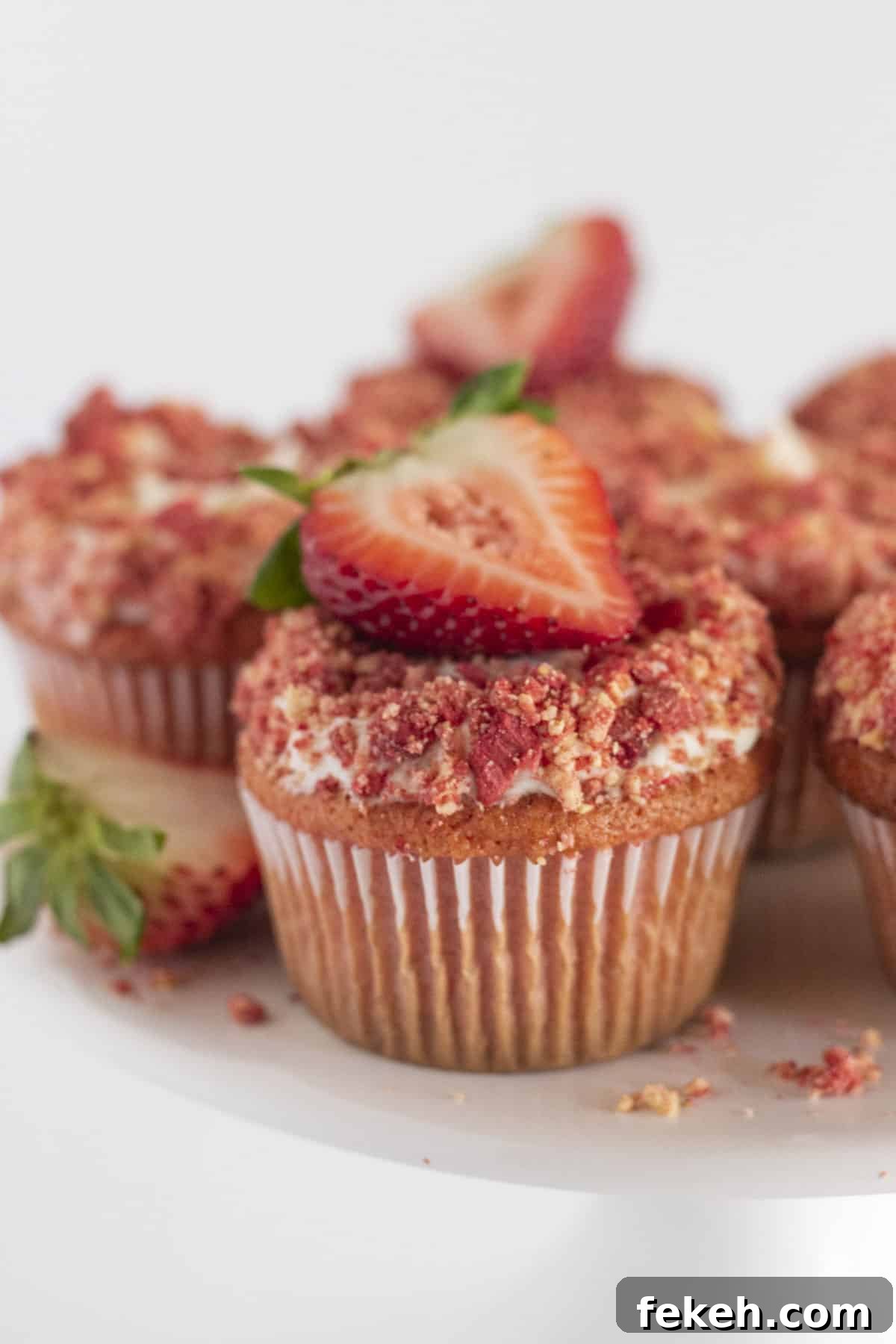 Strawberry Crunch cupcakes on a white cake plate with fresh strawberries on top.