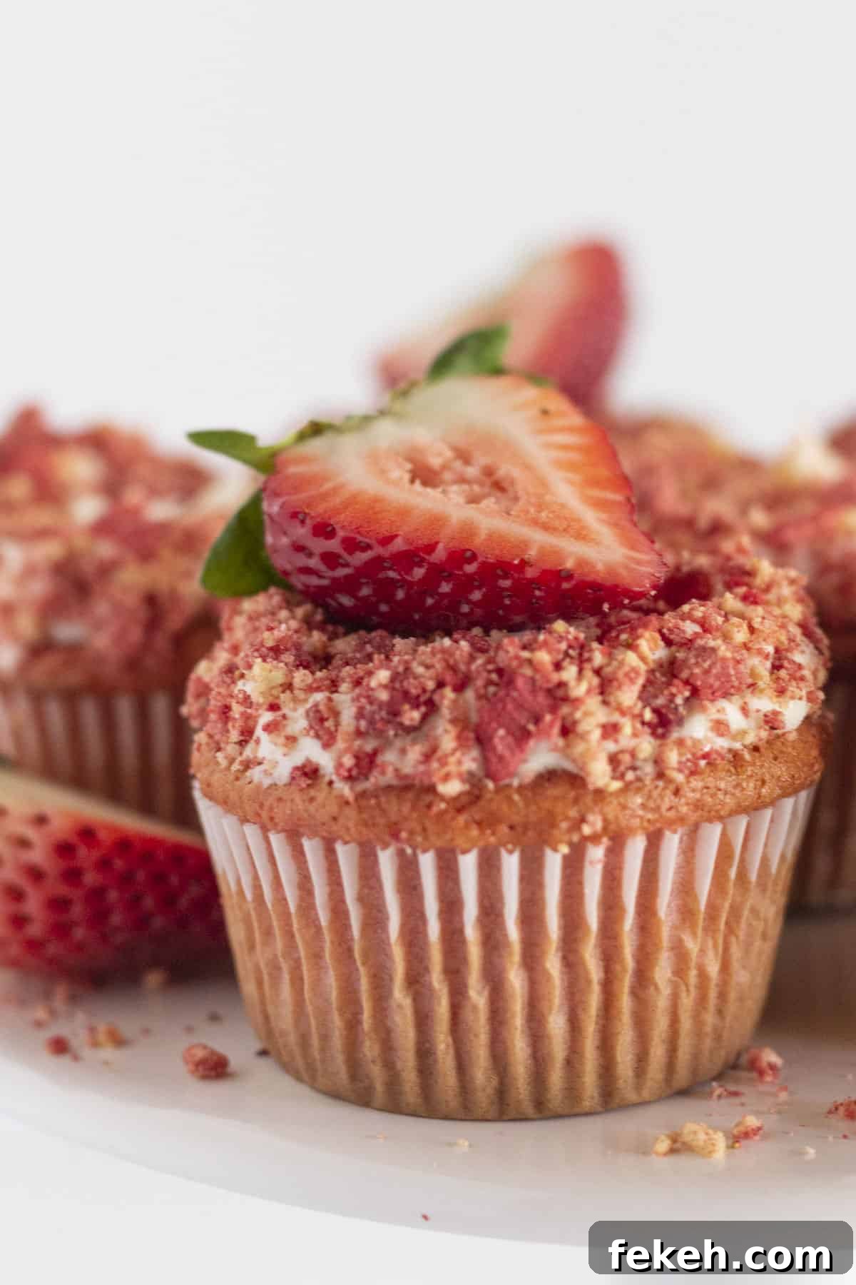A strawberry crunch cupcake with vanilla frosting and fresh strawberries.