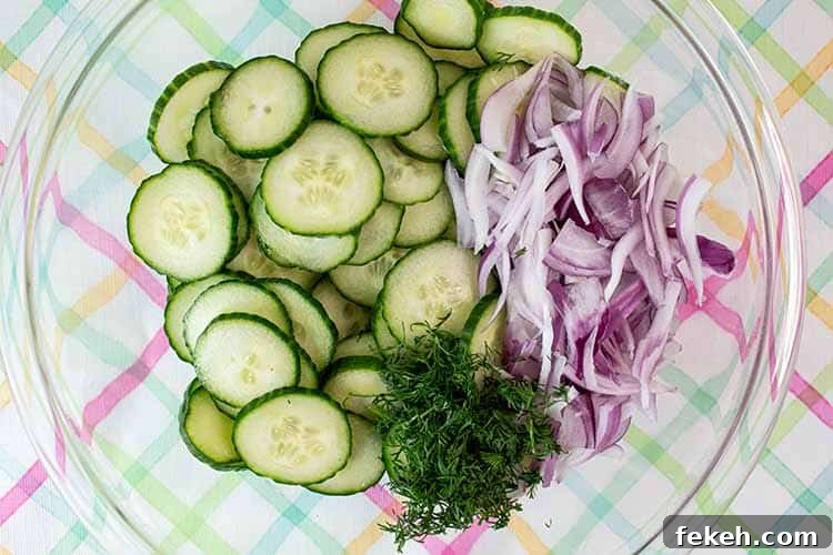 overhead view of cucumber, red onion, and fresh dill in a glass mixing bowl ready to be tossed
