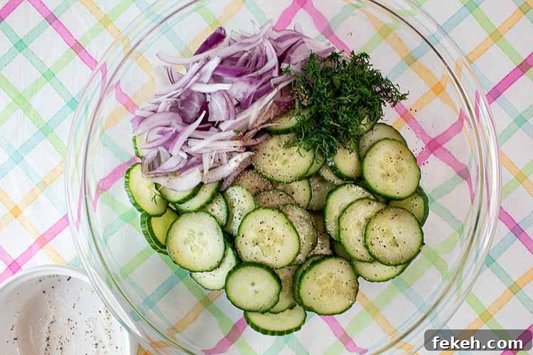 overhead view of cucumber salad dressing added to salad ingredients in glass mixing bowl ready to be lightly tossed