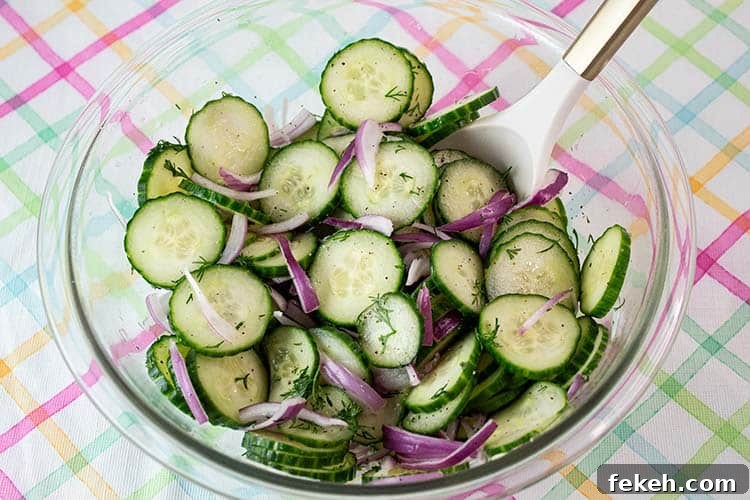 cucumber salad in glass mixing bowl tossed and ready to serve with a white serving spoon