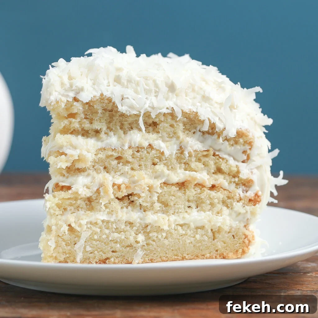 44 Gluten-Free Dairy-Free Cake Recipes for Every Occasion 14 A slice of gluten-free layered coconut cake with white frosting and shredded coconut on top, served on a white plate against a blue background.