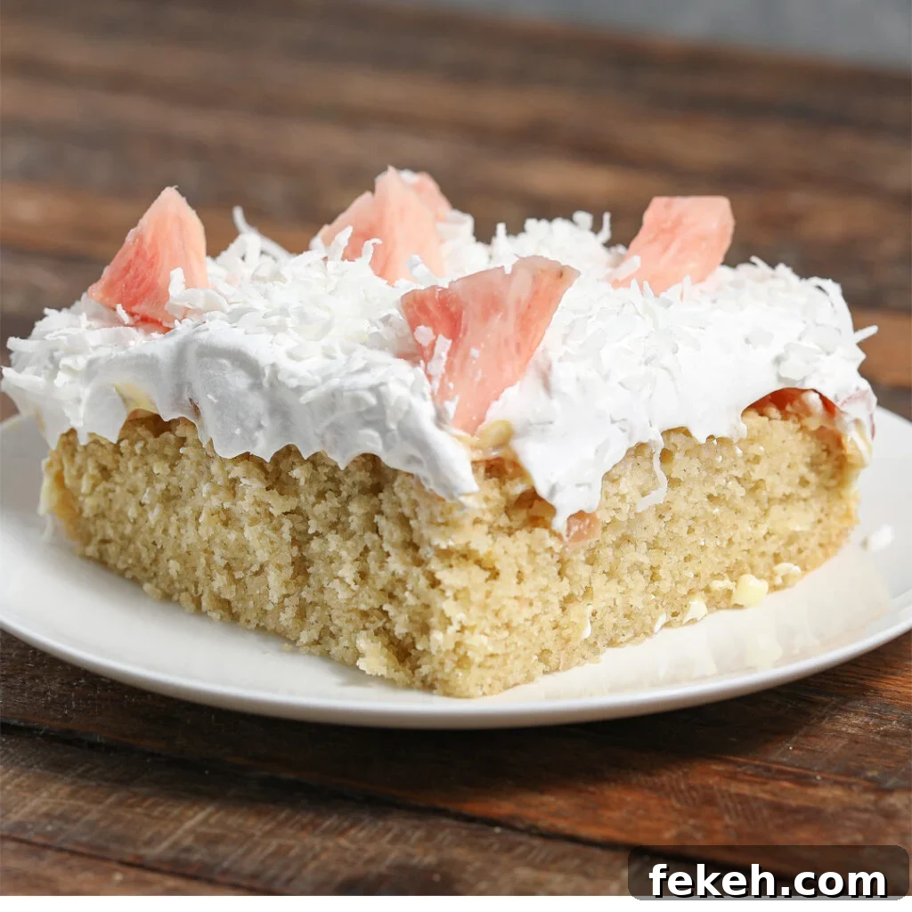 44 Gluten-Free Dairy-Free Cake Recipes for Every Occasion 15 A slice of Pineapple Pudding Cake topped with white whipped cream, shredded coconut, and pieces of pink fruit, served on a white plate on a wooden table.