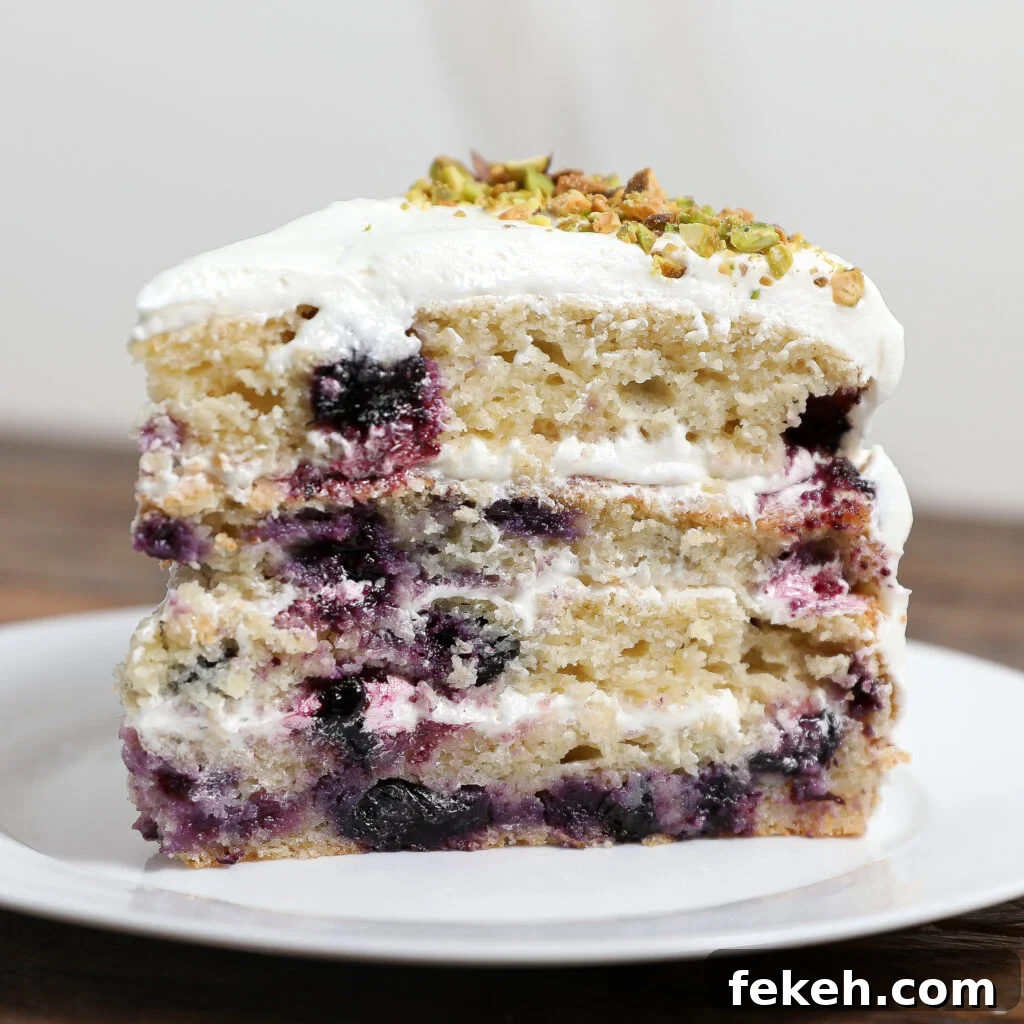 44 Gluten-Free Dairy-Free Cake Recipes for Every Occasion 3 A slice of Lemon Blueberry Cake with white frosting, topped with chopped pistachios, sits on a white plate. The moist cake features visible blueberries and creamy layers, adding a zesty twist to each bite.