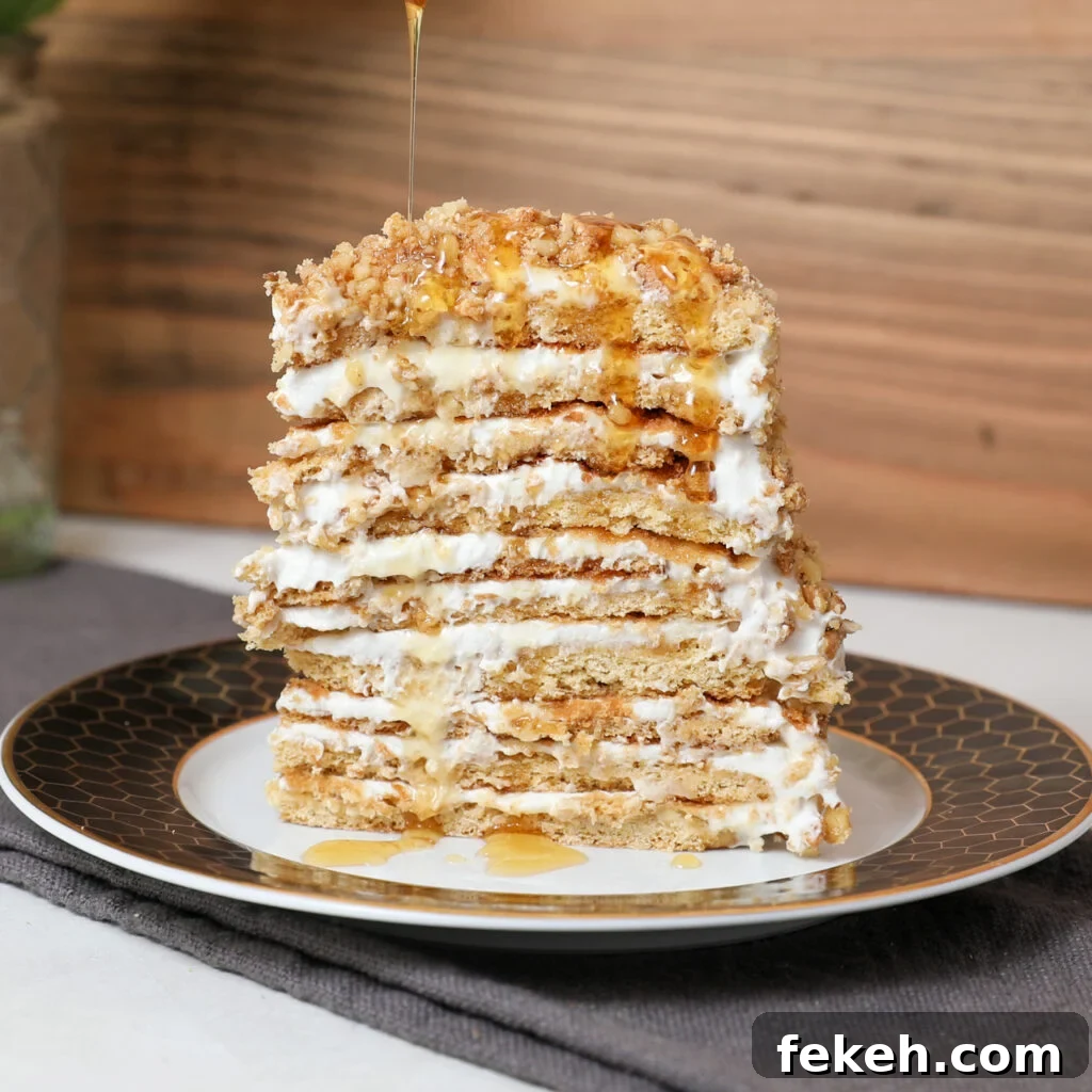 44 Gluten-Free Dairy-Free Cake Recipes for Every Occasion 26 A tall slice of Honey Medovik Cake with cream filling and crumb topping sits on a plate. Honey is being drizzled over the cake, dripping down the sides. The background features a rustic wooden wall.