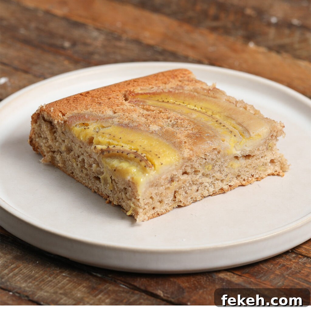 44 Gluten-Free Dairy-Free Cake Recipes for Every Occasion 32 A square piece of banana upside down cake with visible banana slices on top sits on a round white plate, placed on a rustic wooden table.