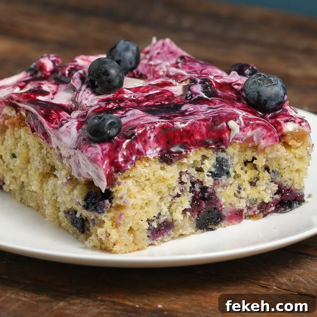 44 Gluten-Free Dairy-Free Cake Recipes for Every Occasion 34 A slice of Lemon Blueberry Poke Sheet Cake topped with creamy purple frosting and fresh blueberries is served on a white plate, sitting on a rustic wooden surface.