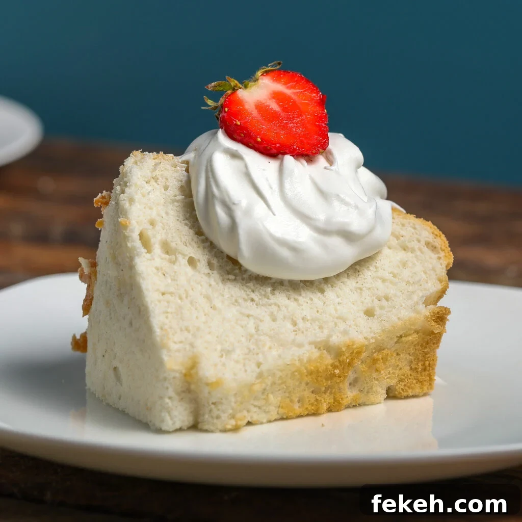44 Gluten-Free Dairy-Free Cake Recipes for Every Occasion 36 A slice of angel food cake topped with a dollop of whipped cream and a halved strawberry, served on a white plate against a blue background.