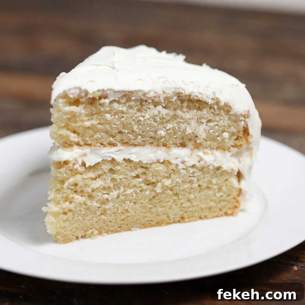 44 Gluten-Free Dairy-Free Cake Recipes for Every Occasion 41 A slice of two-layer White Velvet Cake with white frosting between the layers and on top, served on a white plate on a wooden table.