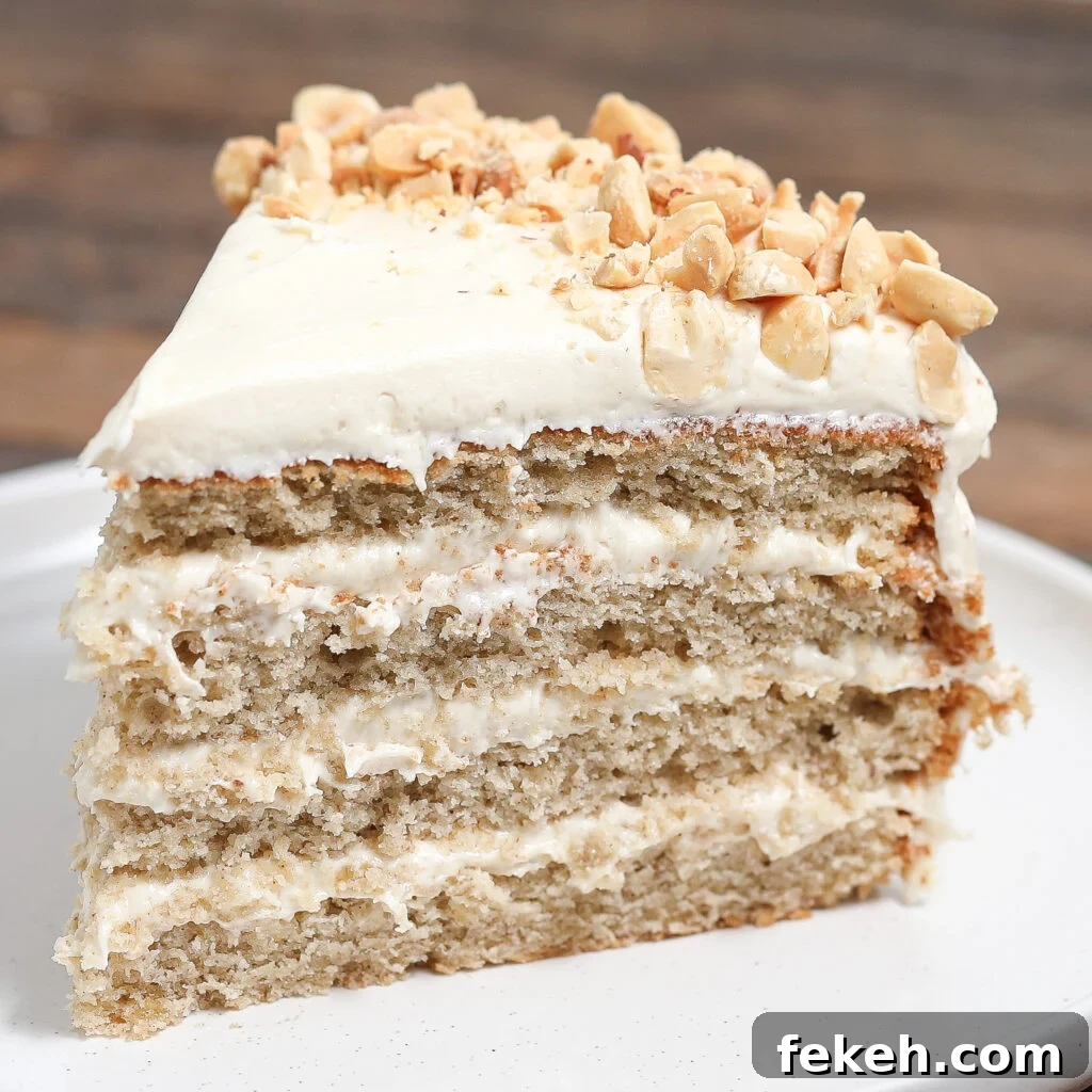 44 Gluten-Free Dairy-Free Cake Recipes for Every Occasion 42 A slice of spiced banana cake with white frosting and chopped nuts on top, served on a white plate with a blurred wooden background.