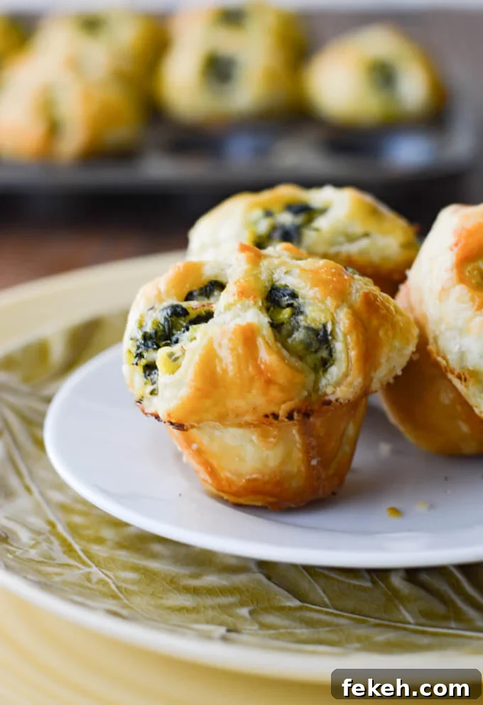 Spinach Puff Pastry Bites: Flaky Savory Appetizer Recipe 2 Three spinach stuffed puff pastry appetizers with more appetizers in a muffin tin in the background.