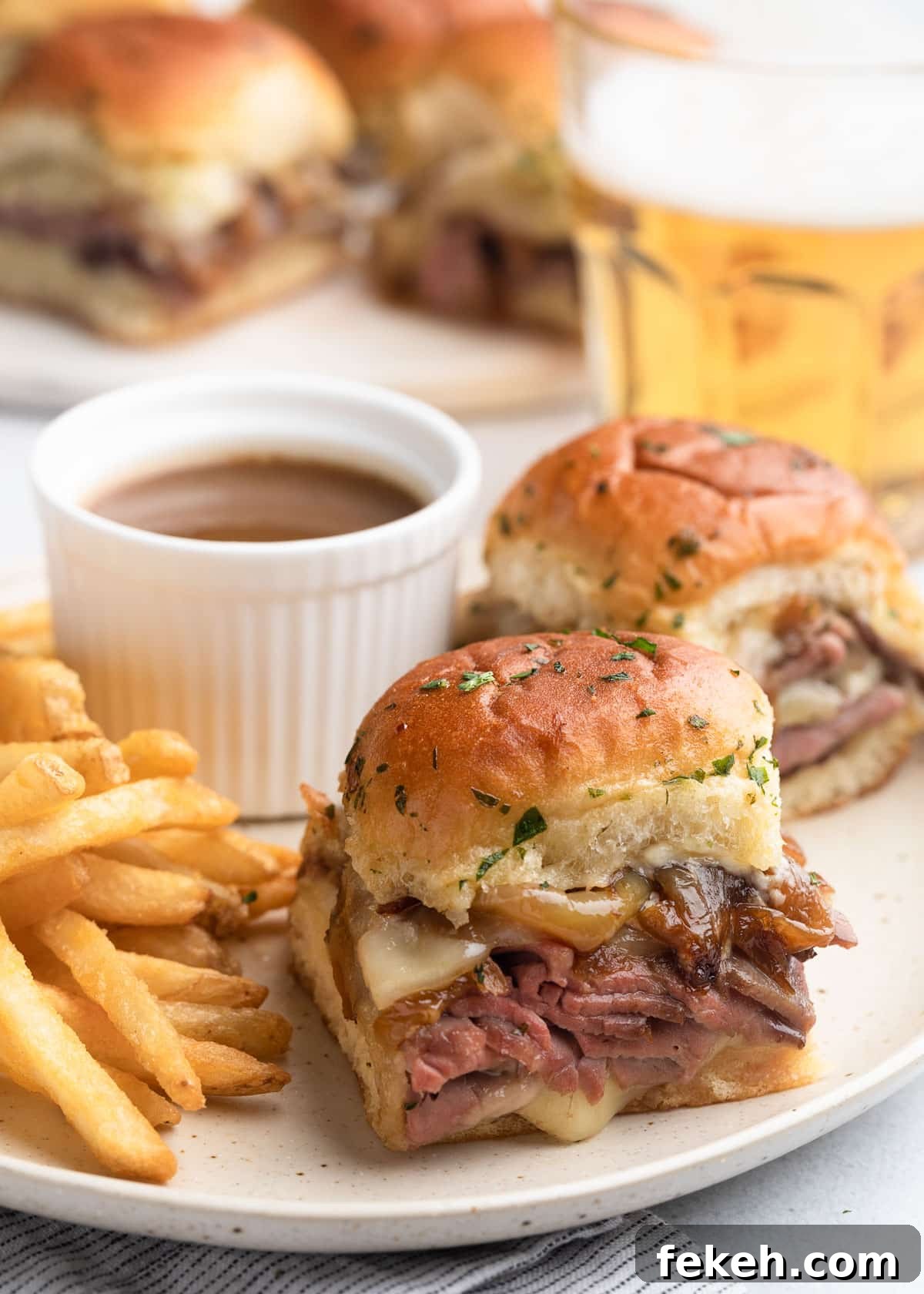 french dip sliders on an ivory ceramic plate with french fries and a cup of au jus