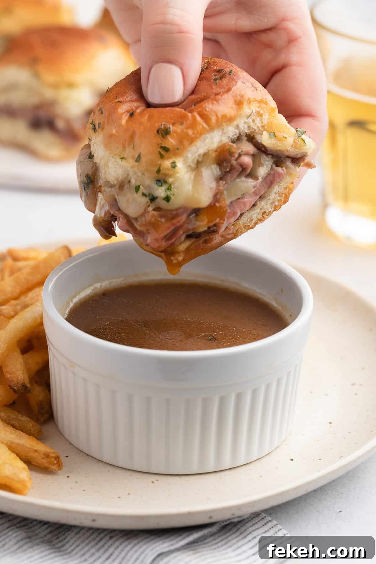 roast beef slider being dipped into a white ramekin of jus
