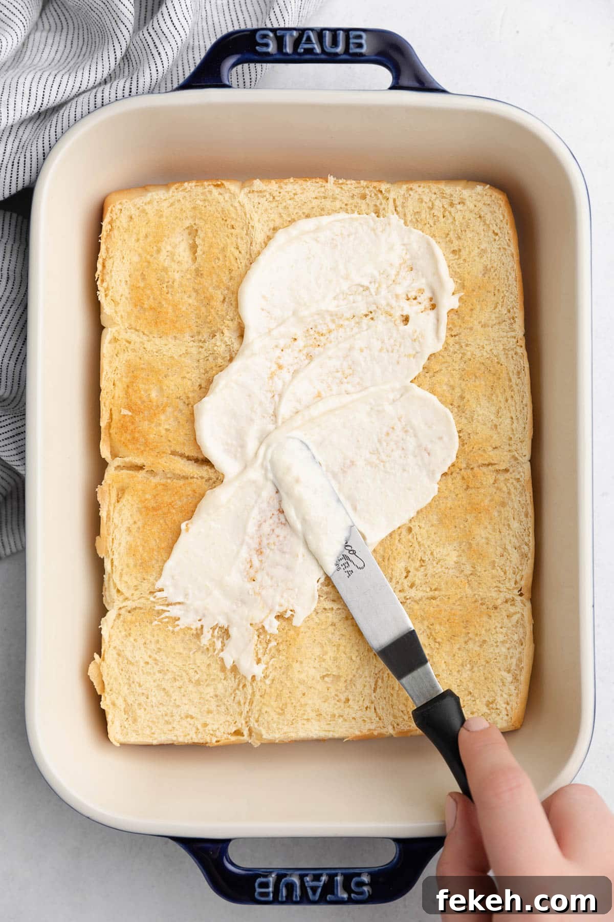 spreading horseradish mayo onto toasted slider rolls in a rectangular baking dish with an offset spatula