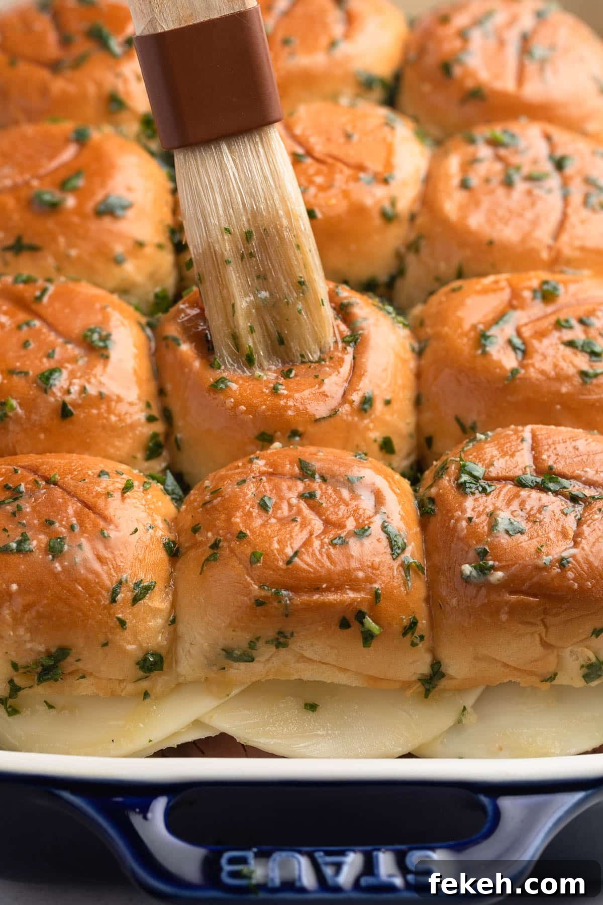spreading butter sauce over French dip sliders in a baking dish with a pastry brush