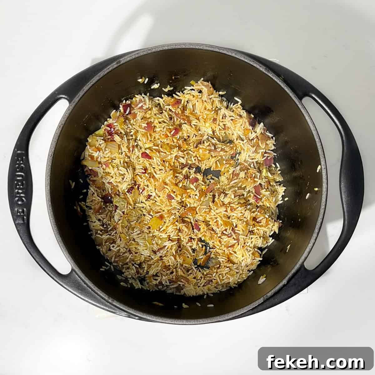 Majestic Moroccan Rice Pilaf with Saffron and Aromatic Spices 7 Mixing rice with spices, oil and onions in a black saucepan.
