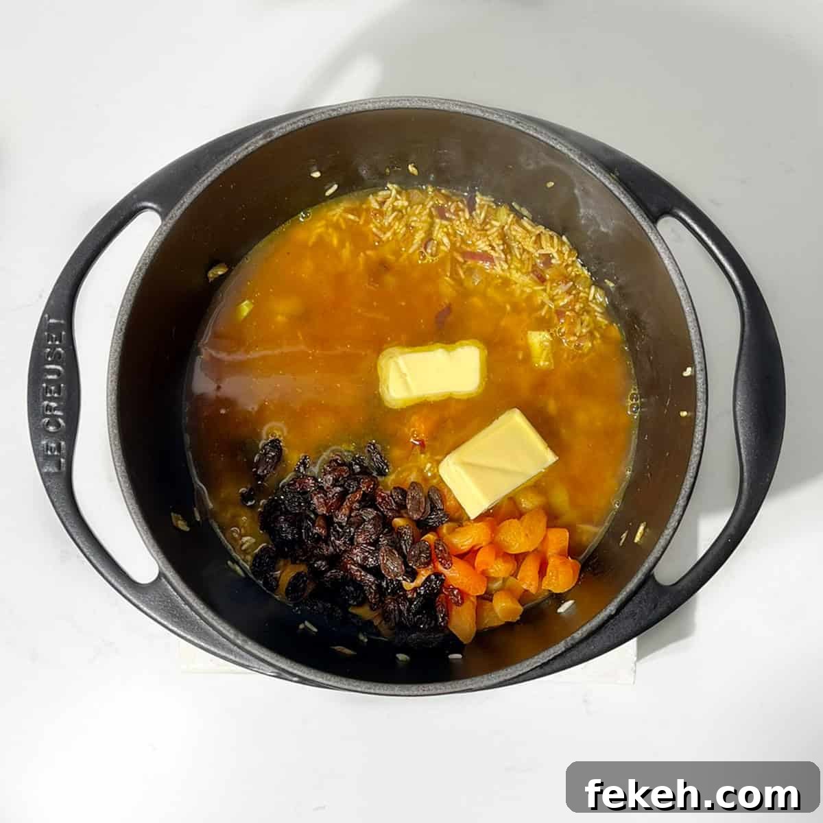Majestic Moroccan Rice Pilaf with Saffron and Aromatic Spices 8 Adding stock and butter and rice in a black cast iron saucepan.