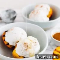 Grilled peaches and coconut ice cream in a bowl with maple syrup drizzled on top.
