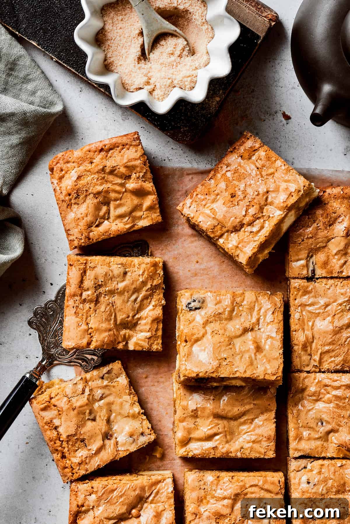 This sweet and irresistible Blonde Brownies recipe features blondies studded with white chocolate chips and crunchy pecans. A cutting board of blonde brownie squares with a bowl of brown sugar next to it.
