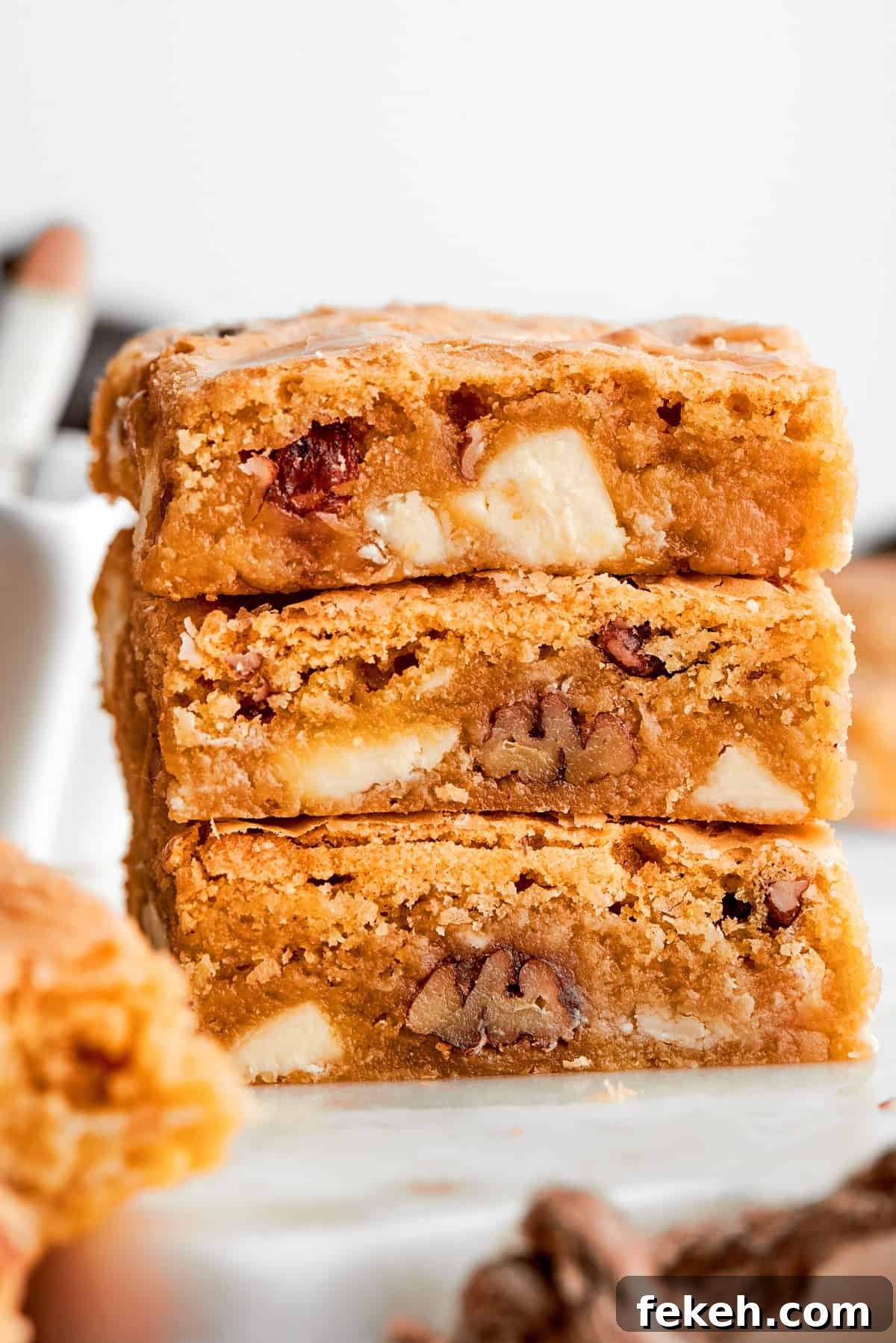 This sweet and irresistible Blonde Brownies recipe features blondies studded with white chocolate chips and crunchy pecans. A stack of three blonde brownies with white chocolate chips and pecans visible.