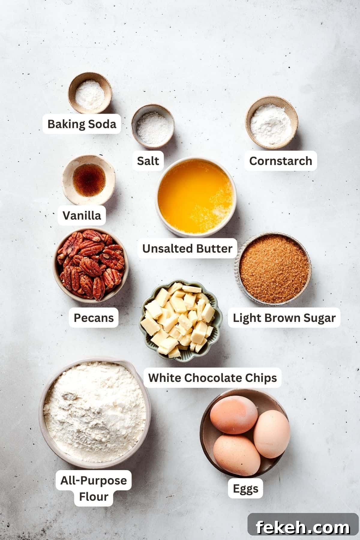 This sweet and irresistible Blonde Brownies recipe features blondies studded with white chocolate chips and crunchy pecans. The ingredients for blonde brownies are shown portioned out: flour, cornstarch, baking soda, salt, vanilla, brown sugar, melted butter, eggs, pecans, white chocolate chips.