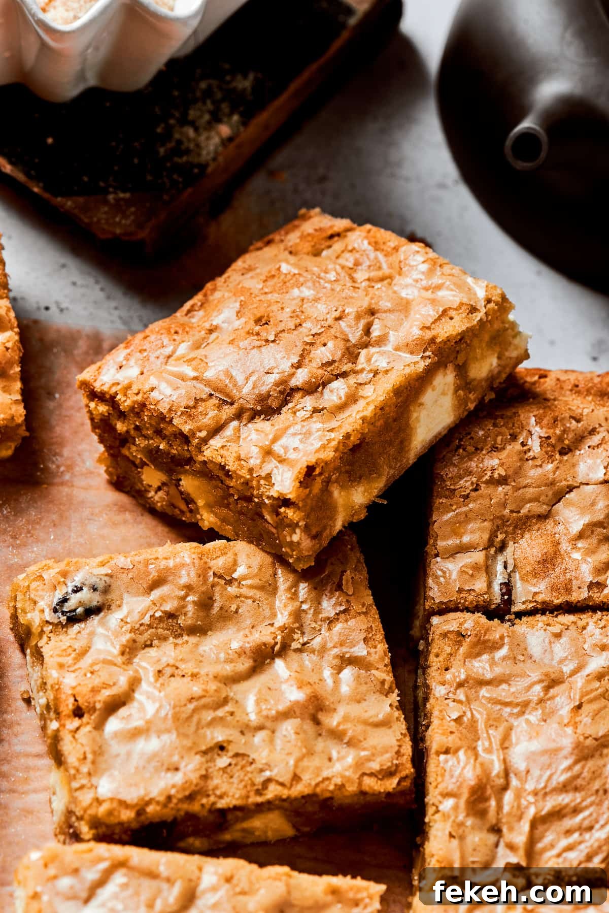 This sweet and irresistible Blonde Brownies recipe features blondies studded with white chocolate chips and crunchy pecans. A side view of a blonde brownie on top of more brownies.