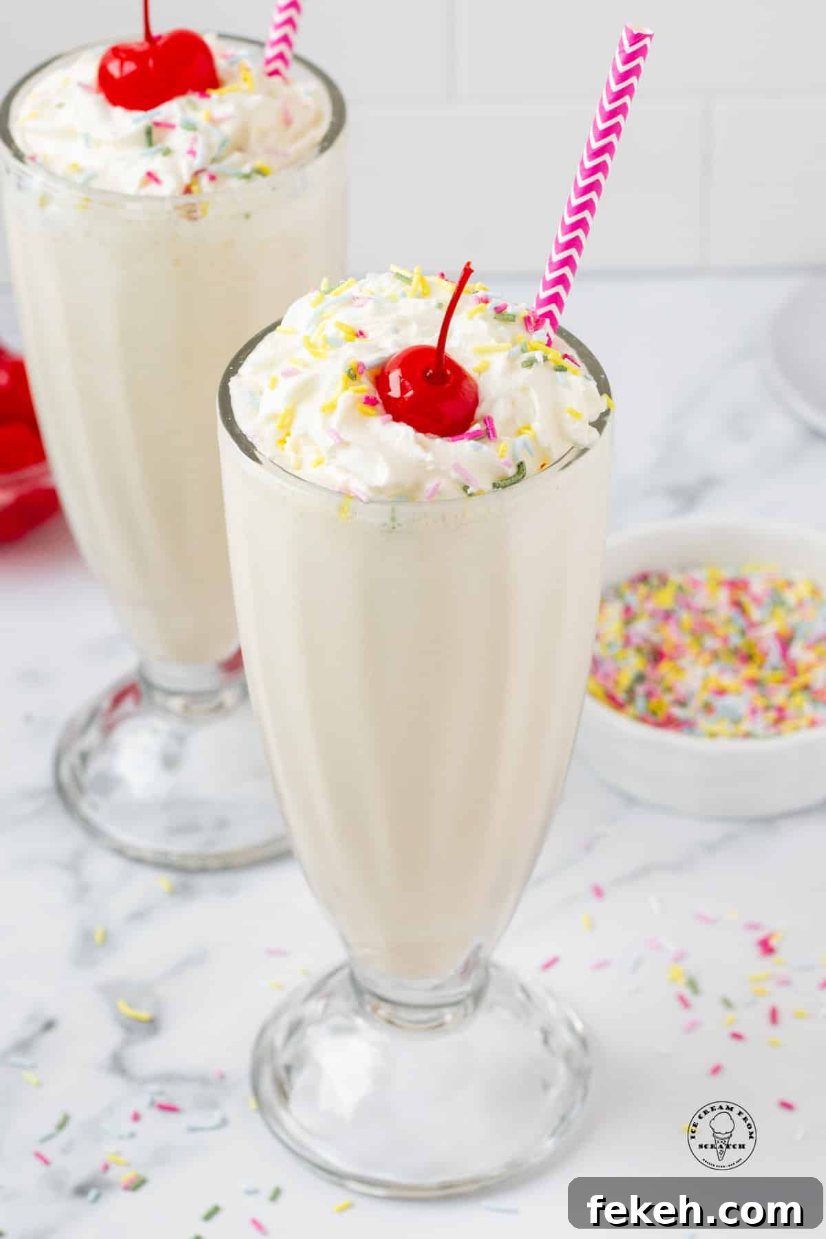 Classic Vanilla Milkshake Recipe: Creamy Homemade Shake in Minutes 6 two vanilla milkshakes with purple straws, topped with whipped cream, sprinkles, and cherries