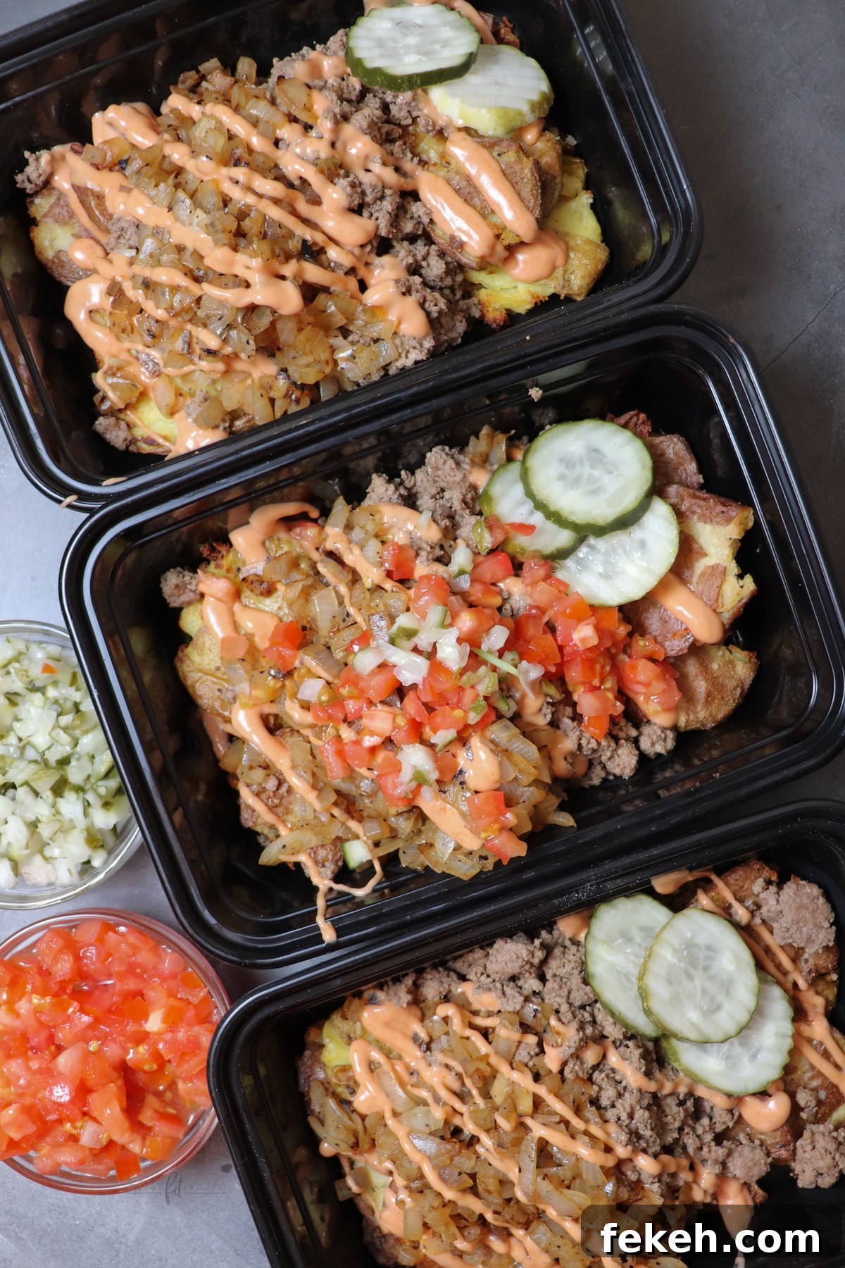 Animal-Style Burger Bowls: Low-Carb Cheeseburger Skillet Bowl 2 Animal style burger bowls showing meal prep containers loaded with smashed potatoes, ground beef, caramelized onions, topped with pickles, diced onions, tomatoes, and sauce.