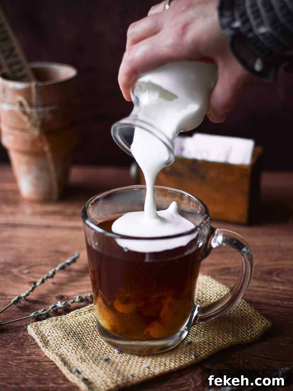 Angled view of frothed milk being poured into a glass with tea to make a lavender tea latte.