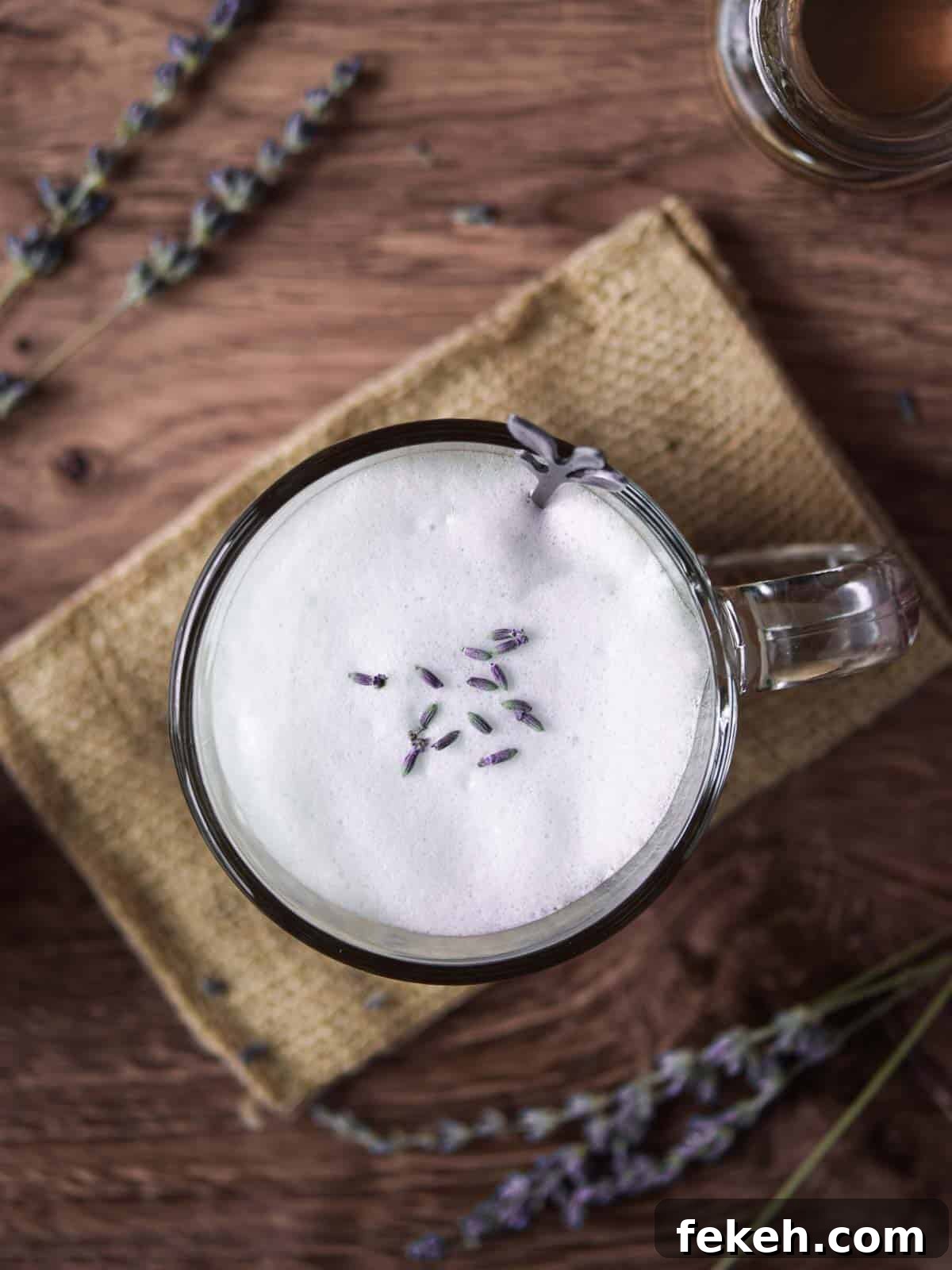 Overhead of a lavender tea latte on a wood background with lavender sprigs.