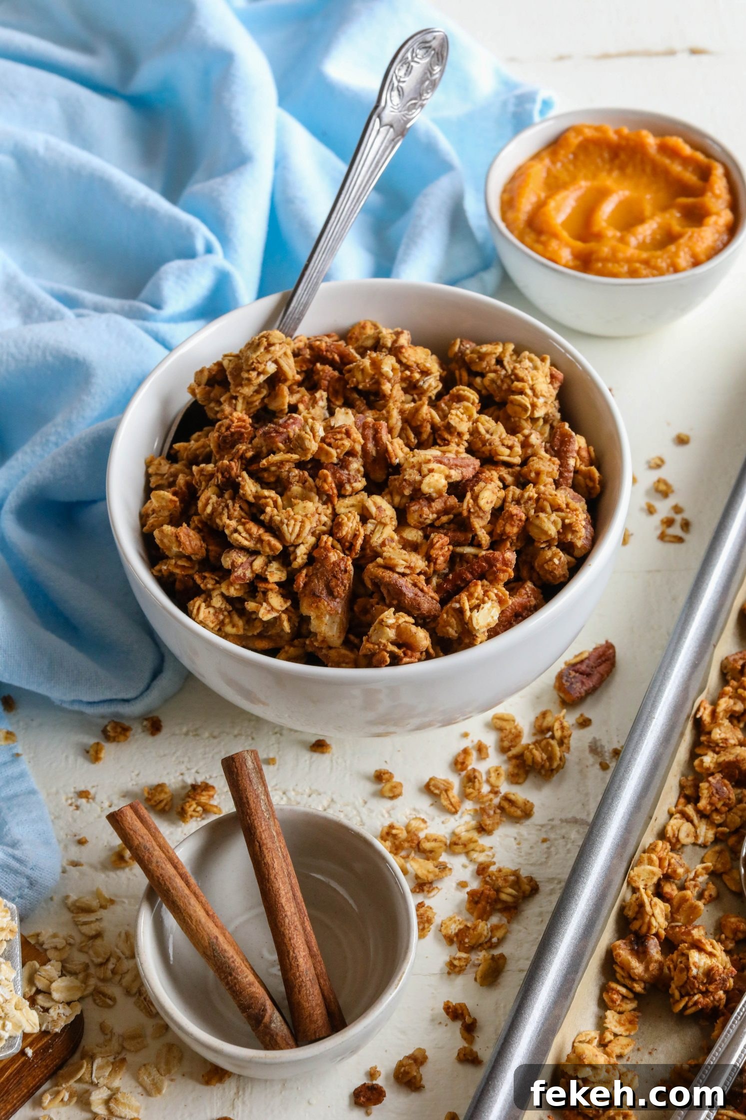 Sweet Potato Spice Granola Recipe for Cozy Fall Mornings 8 Sweet Potato Spice Granola served in bowl with a spoon and sweet potato puree on the side with blue towel and cinnamon