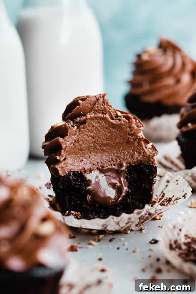 Nutella Chocolate Cupcakes with Cream Cheese Nutella Frosting 2 A nutella cupcake with a bite missing, revealing creamy nutella filling in the center.