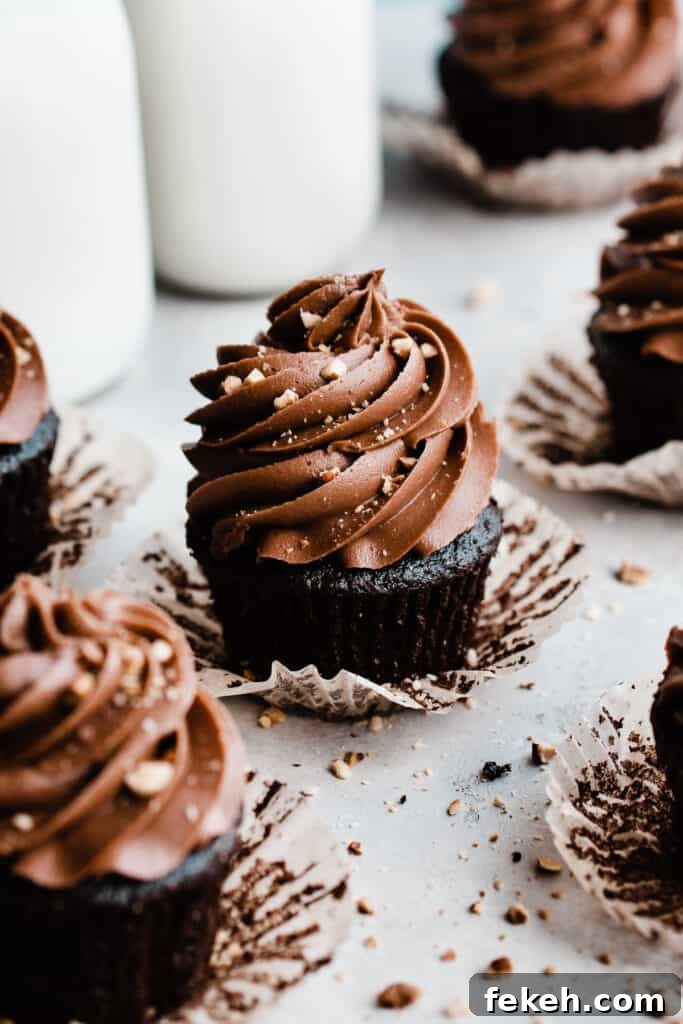 Nutella Chocolate Cupcakes with Cream Cheese Nutella Frosting 9 Nutella cucpakes with the wrappers peeled back on a gray surface, topped with crushed hazelnuts.