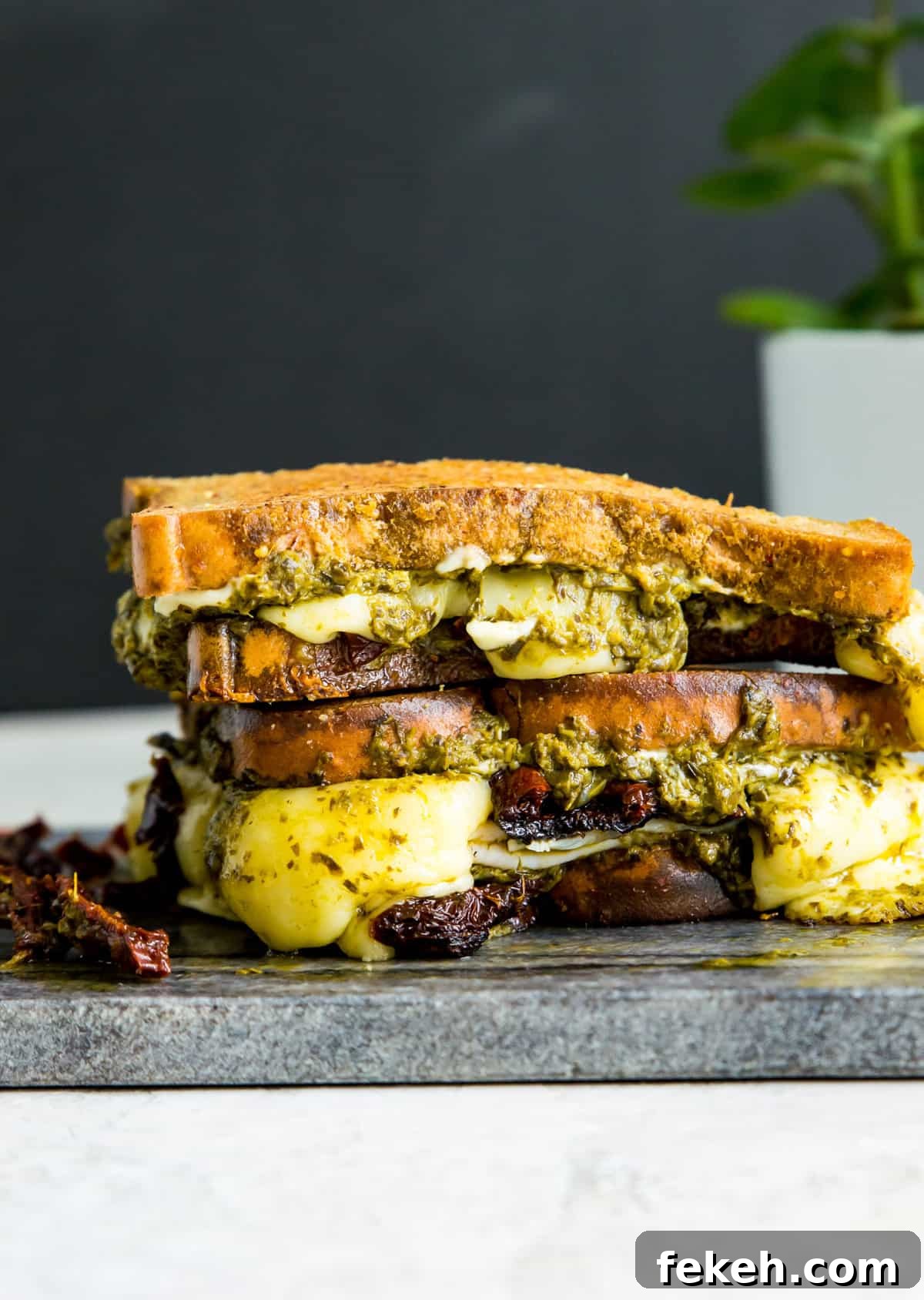 Grilled Turkey and Pesto Sandwich Recipe 2 A sandwich with turkey, sun dried tomatoes, mozzarella cheese and pesto in it that is cut in half and stacked on a cutting board.