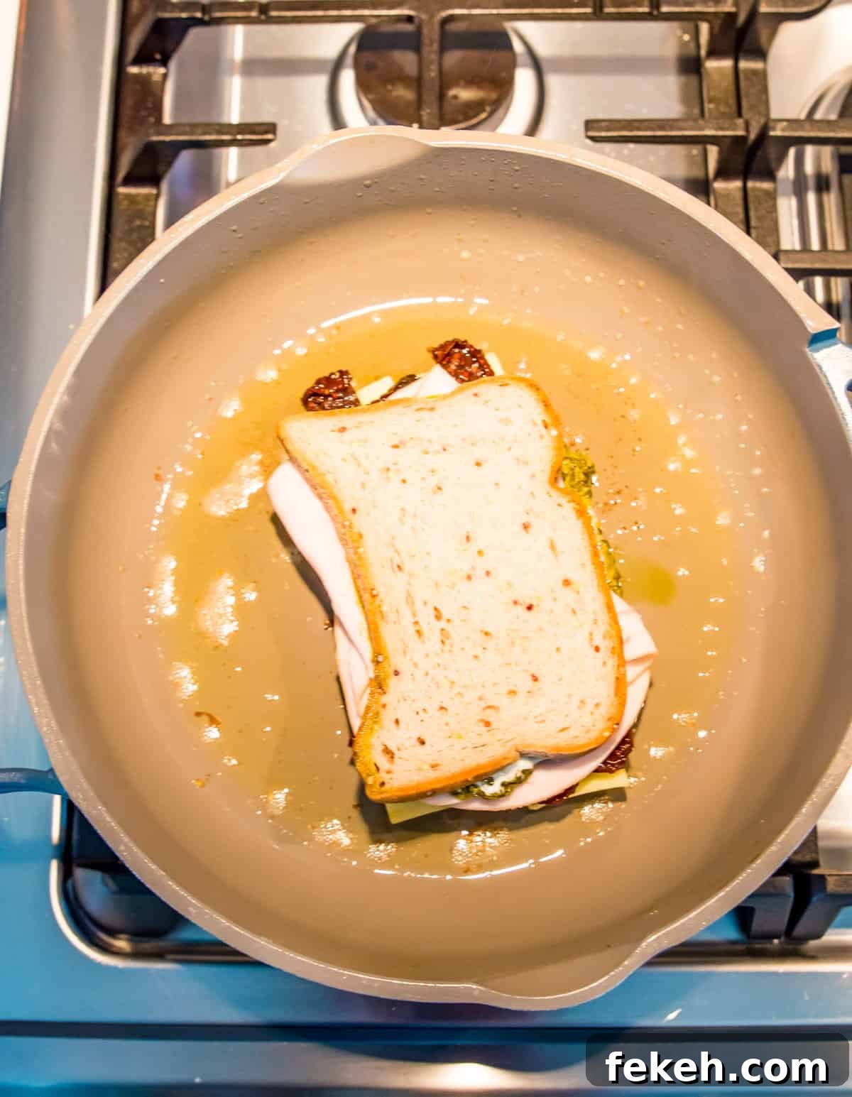 Grilled Turkey and Pesto Sandwich Recipe 6 A sandwich cooking in a pan on the stovetop.