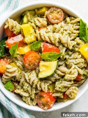 A bowl of veggie pesto pasta with chopped baby tomatoes and basil leaves on top.