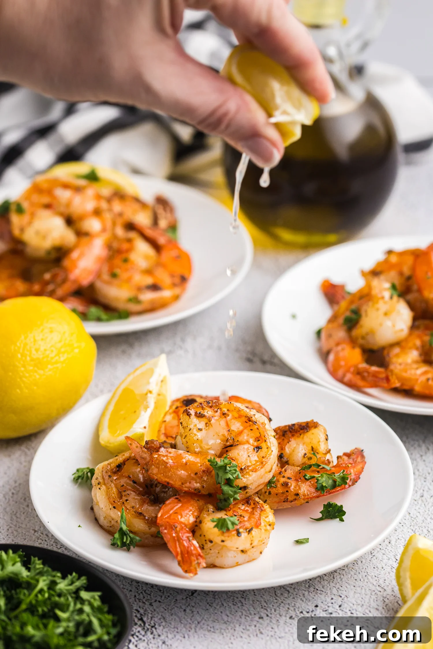A hand squeezing fresh lemon juice over a plate of seasoned, grilled shrimp.