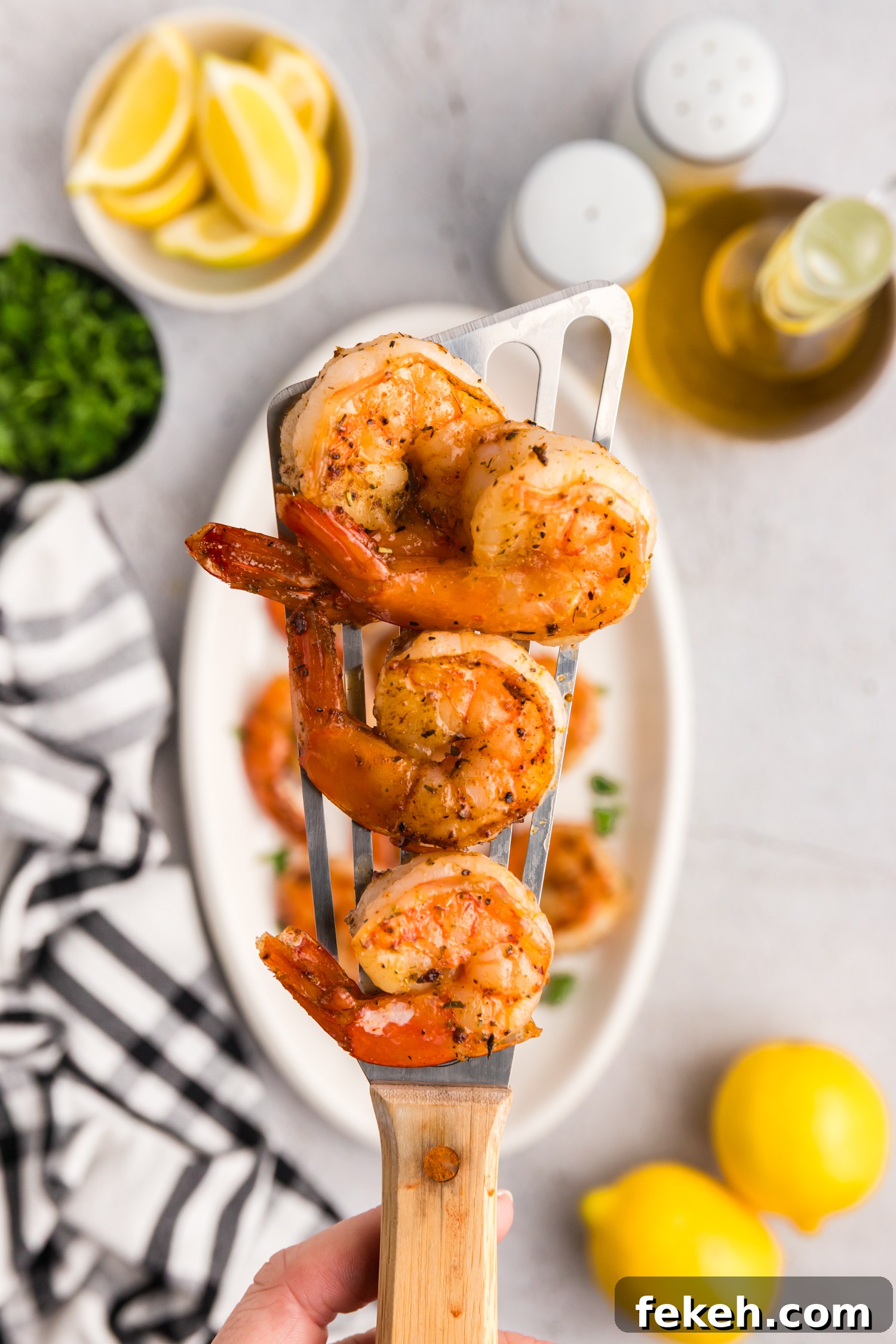 Cooked shrimp resting on a metal spatula held above a serving plate with parsley garnish.