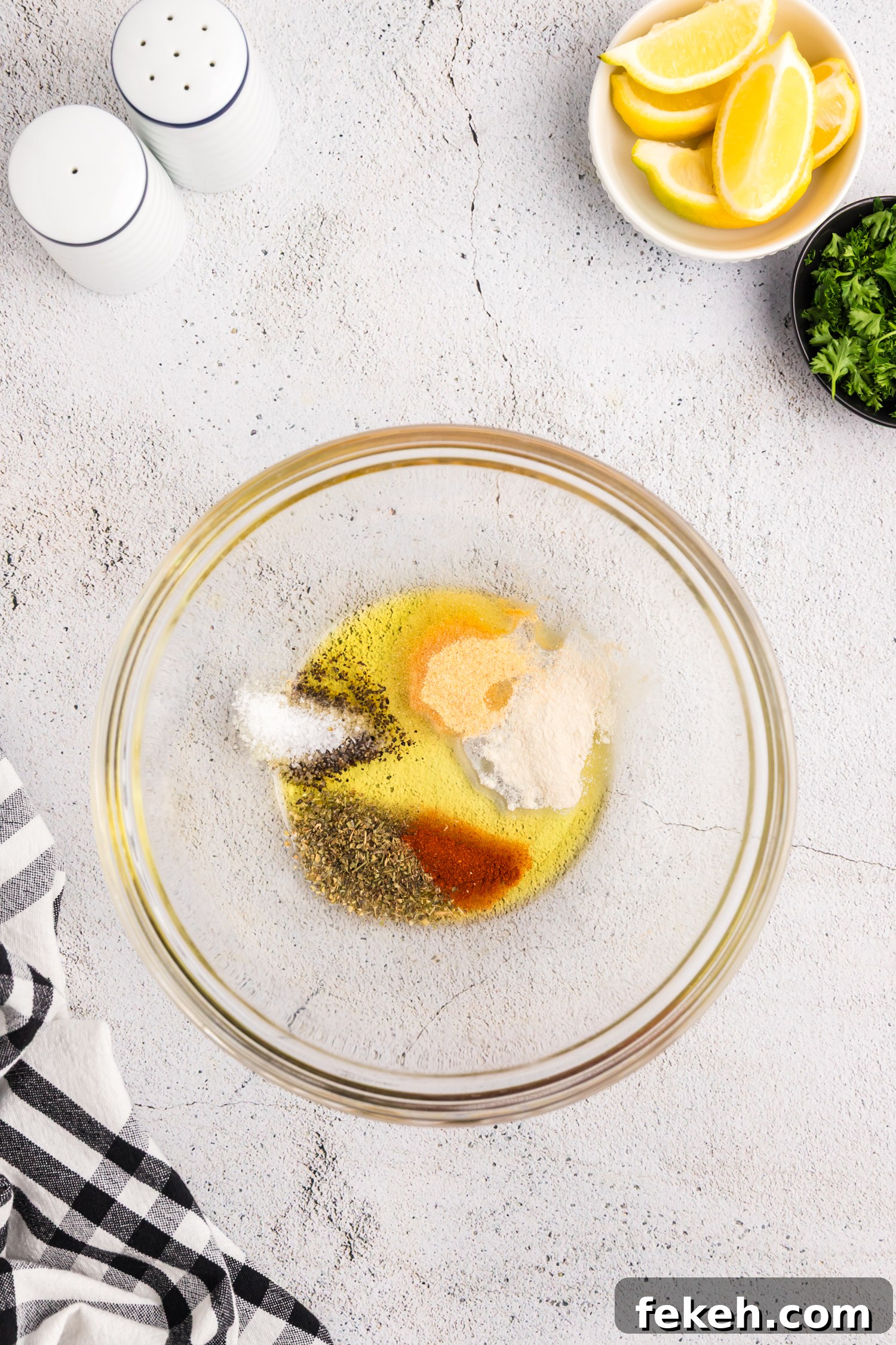 A glass bowl containing olive oil and a variety of seasonings, including paprika, salt, pepper, garlic powder, and herbs.