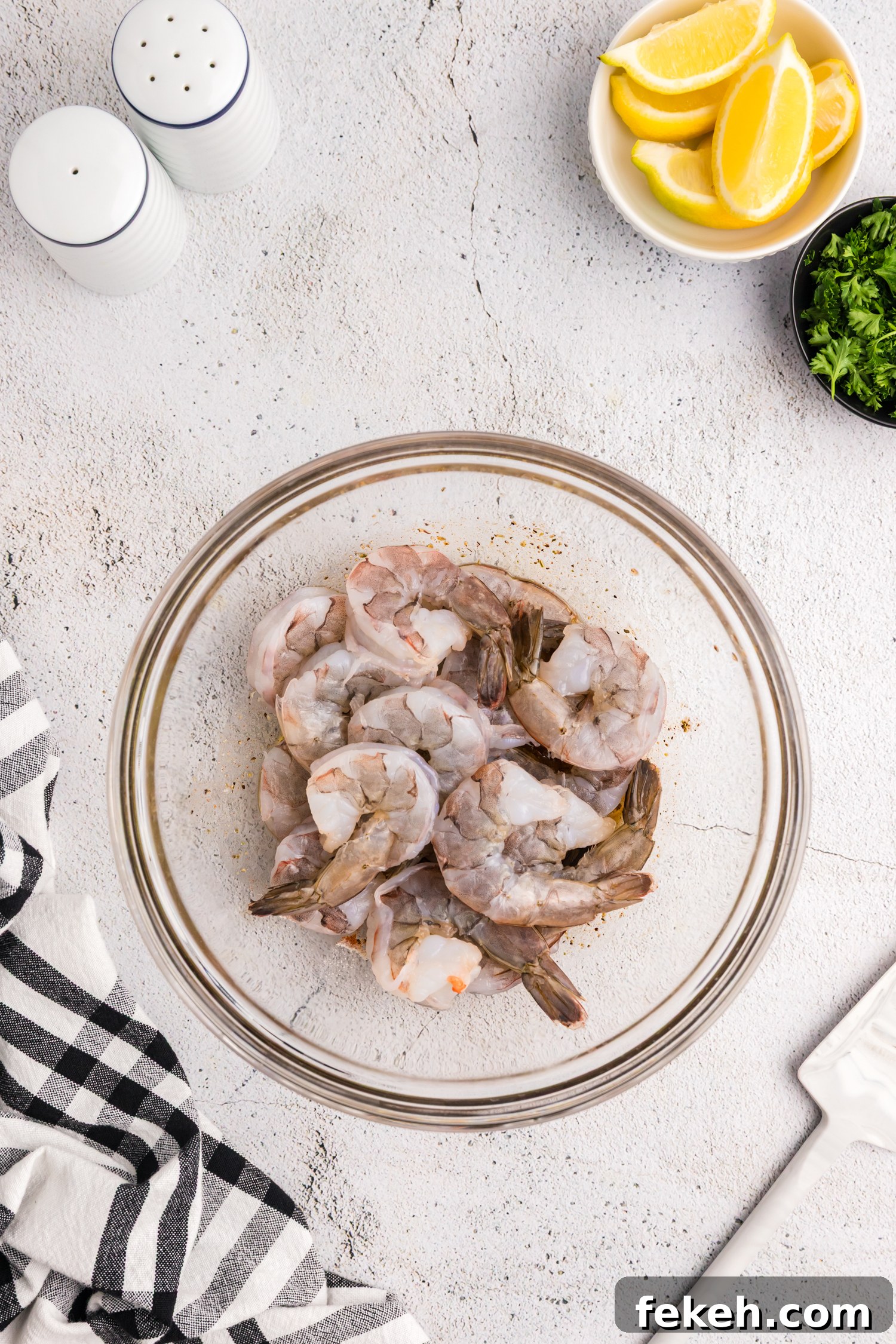 Raw shrimp added to a bowl with marinade at the bottom, about to be mixed.