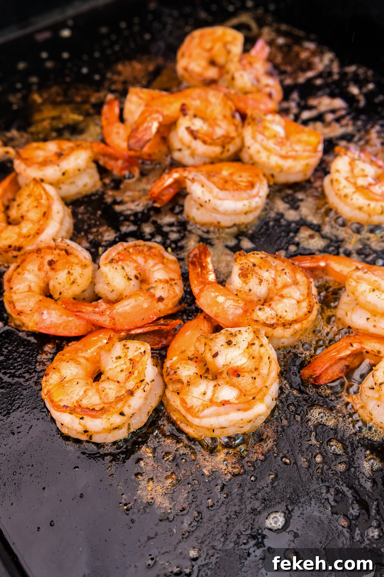 Close-up of shrimp on a flat-top griddle, fully cooked to a golden brown with slightly curled edges.