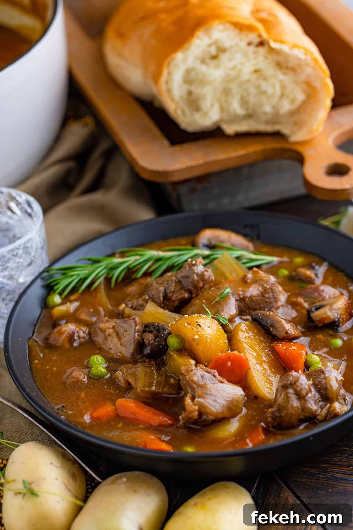 Venison Stew in black bowl garnished with rosemary and bread in background.