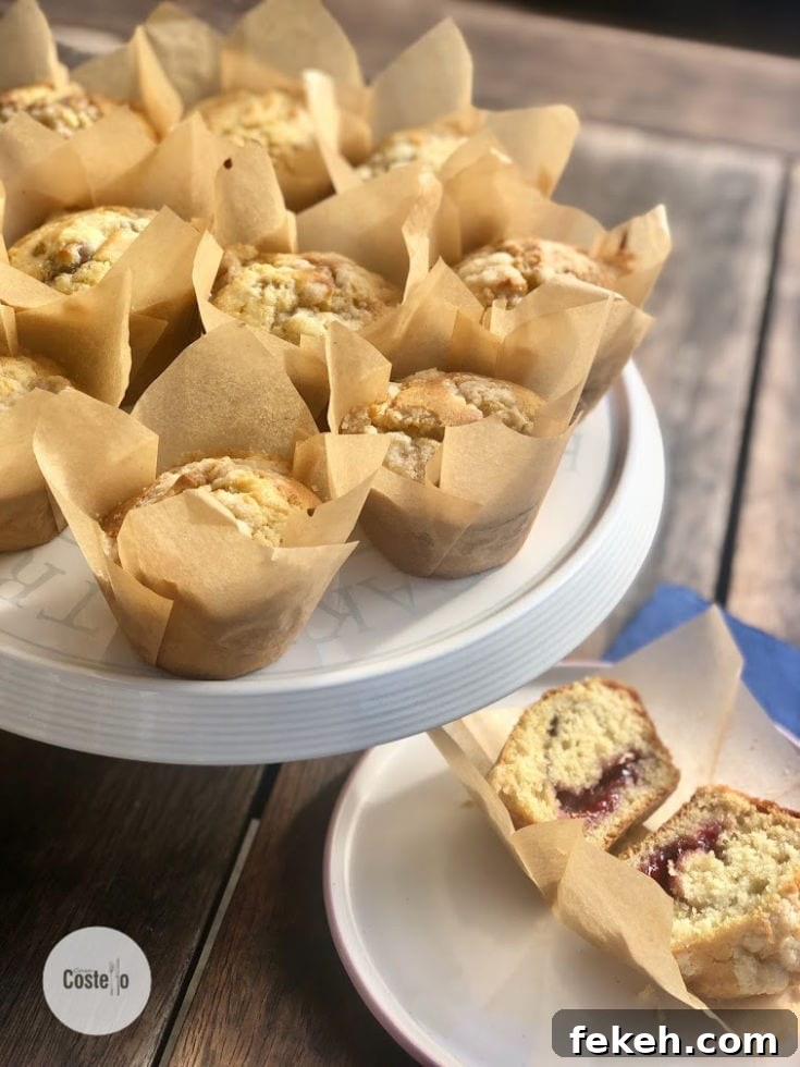 Jam-Filled Muffins with Crunchy Streusel Topping 3 Jam Muffins in Paper cases arranged on a stand. One muffin chopped in half displaying a jam centre.