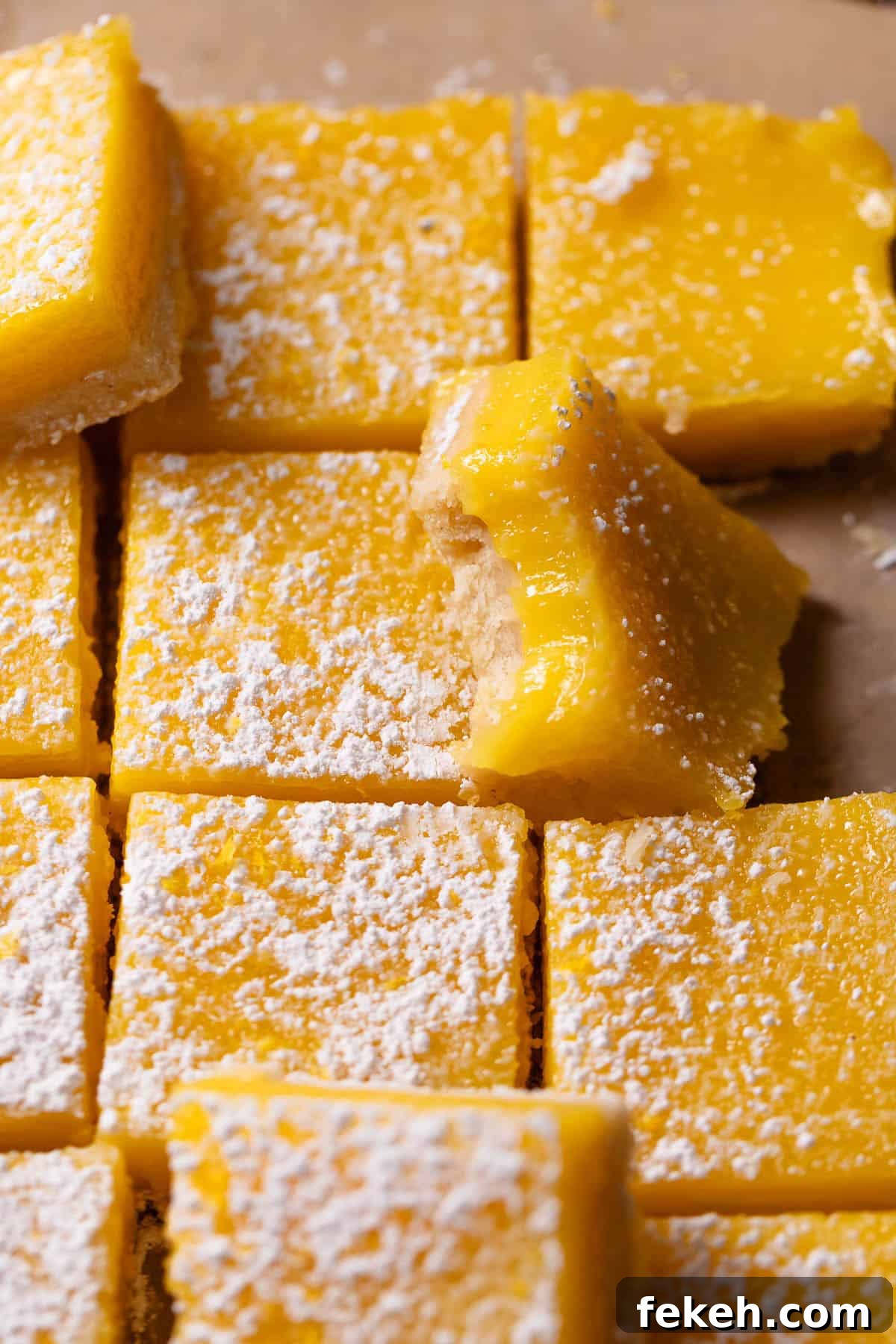 Lemon bars dusted with powdered sugar with one missing a bite.