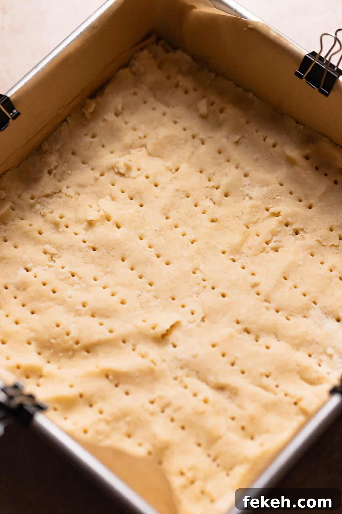 Shortbread dough pressed into a square pan pricked with a fork before baking.