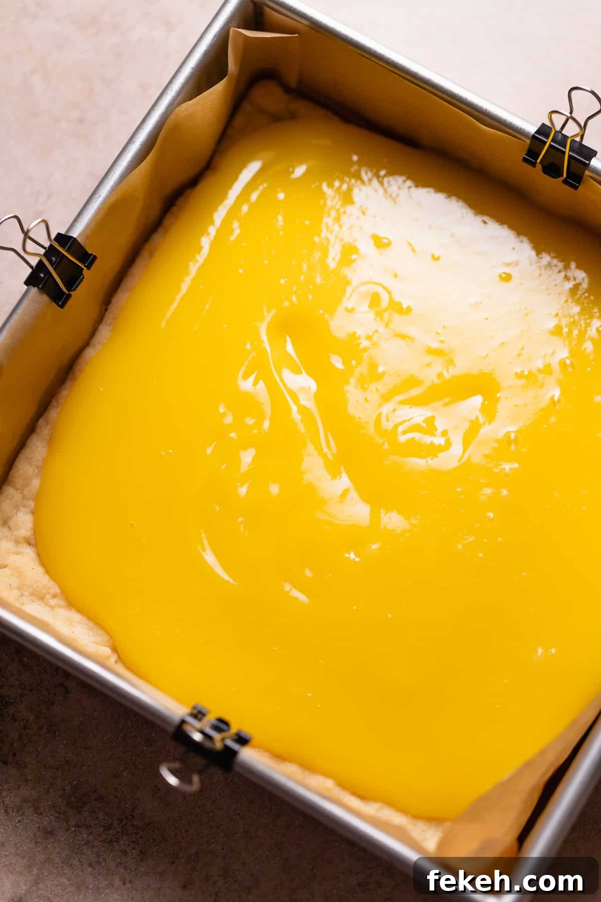 Lemon curd being spread over the top of the baked shortbread crust.