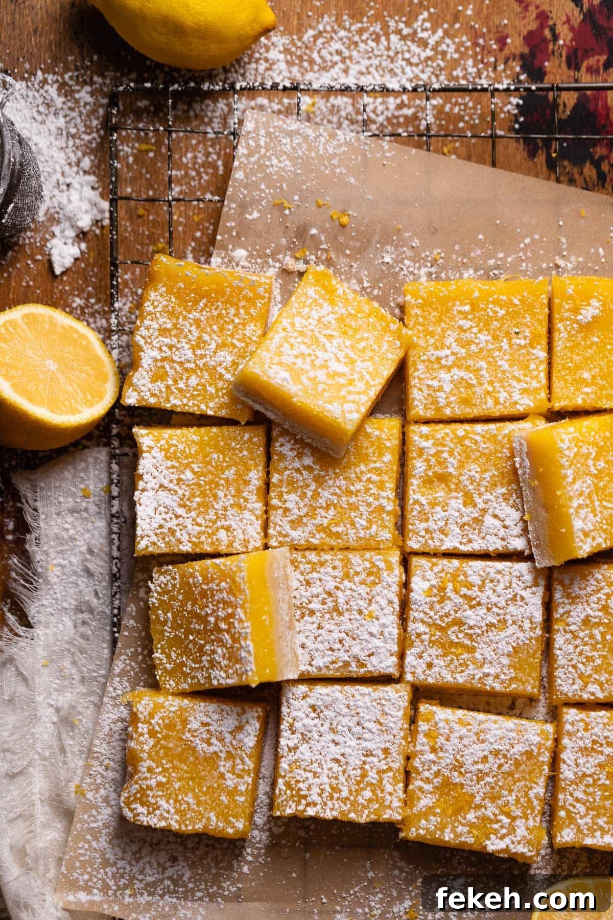 Lemon bars cut into squares and dusted with powdered sugar on brown parchment paper.