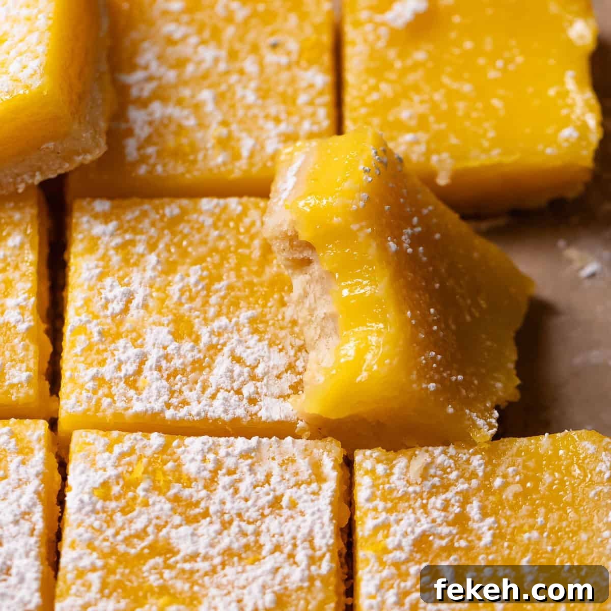Lemon bars dusted with powdered sugar with one missing a bite.