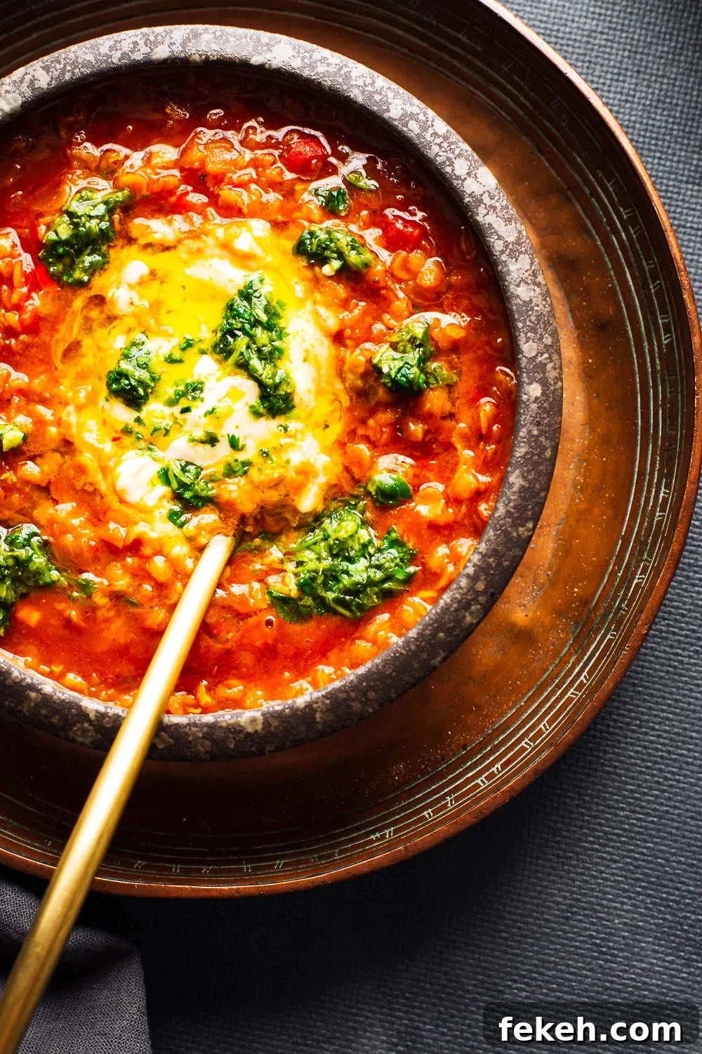 Spicy Harissa Lentil Soup with Fresh Cilantro Salsa 6 A bowl of red lentil soup with yoghurt and green chilli salsa and a gold spoon.