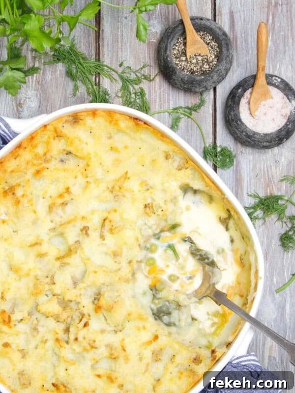 Cheesy Potato Pie Recipe: Crispy Crust & Melty Filling 16 Fish pie being served with silver spoon on a wooden table. There is parsley to accessorise the table, along with small pots of of salt and pepper.